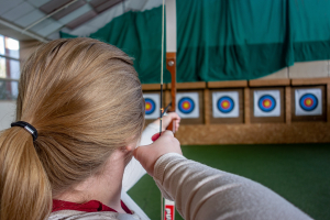 An archer stretches her bow while taking aim at the target